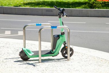 Güneşli bir günde arka planda yeşil bir çimenliği olan kaldırıma park etmiş elektrikli bir scooter.