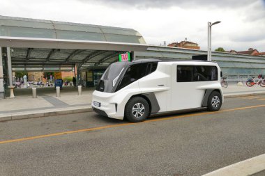 Bir istasyon binasının önüne park edilmiş beyaz bir ETIOCA full elektrikli minivan taksisinin görüntüsü