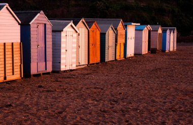 Gün batımında Teignmouth sahilinde bulutlu gökyüzü arka planına karşı bazı plaj kulübeleri.