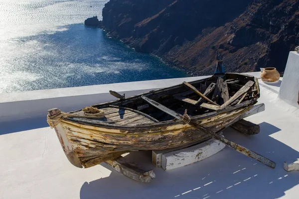 桑托里尼一座白色建筑顶上的一艘蓝色海的旧木船 — 图库照片
