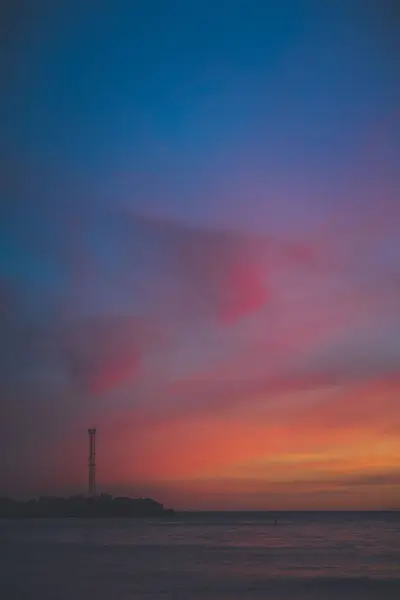 ビーチの灯台に対して静かな海の上に美しい夕日の垂直ショット — ストック写真