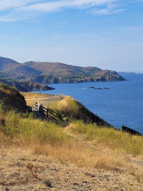 Mavi bulutlu gökyüzünün altında, bir uçurumun kenarındaki küçük tahta köprünün dikey görüntüsü.