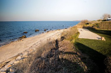 Huzurlu kumlu sahil manzarası ve sakin mavi denizde kayalar
