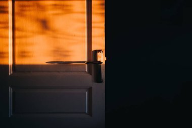Altın güneş ışığının altında, karanlık ve boş bir odanın penceresinden parlayan eski bir kapı.