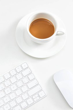 Bir klavye ve bilgisayar faresinin yanında beyaz bir fincan kahve.