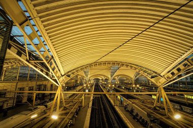 Akşamları Leuven tren istasyonunun geniş açılı bir görüntüsü. İnsanlar ulaşımı bekliyor.