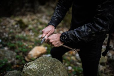 Bıçaklı, siyah paltolu bir adam ağaç dalı kesiyor.