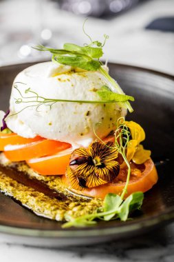 Burrata peyniri ve bulanık arka planda yeşillikler olan bir tostun dikey yakın çekimi.