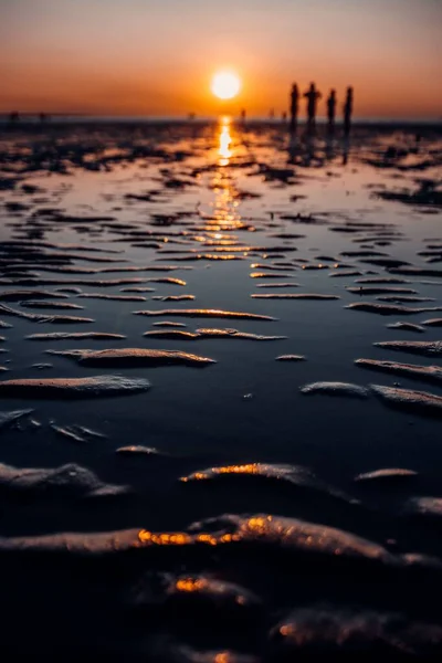 背景に人々のシルエットと日没時の砂浜の垂直ショット — ストック写真