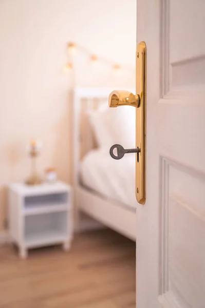 stock image A vertical closeup shot of a white open door with a key in it with a bedroom in a blurry background.