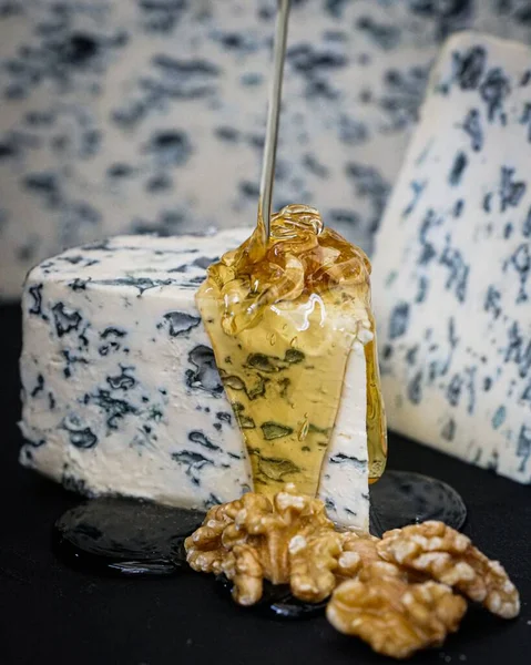一片蜂蜜倒在核桃旁边的蓝色奶酪上 — 图库照片