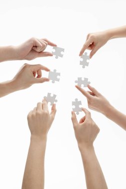 Beyaz bir arkaplan önünde yapboz parçalarını tutan ellerin dikey görüntüsü