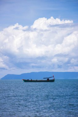 Mavi bulutlu gökyüzünün altındaki küçük teknenin dikey yan görüntüsü