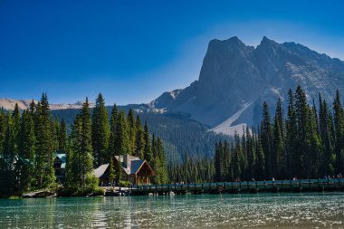 Banff ve Jasper Ulusal Parkı 'ndaki göl kenarındaki ağaçların ve evlerin olduğu güzel bir dağ manzarası.