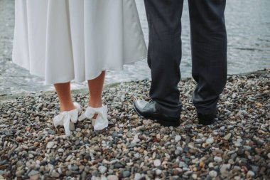 Bir damat ve bir köprü sahilde gün ışığında küçük çakıl taşları üzerinde duruyor.