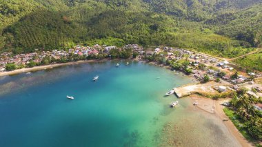Çimlerle kaplı tepelerle çevrili küçük bir sahil kasabasının yüksek açılı görüntüsü.