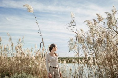 Uzun kamışların yanında poz veren genç ve şık bir dişi göl kıyısında büyüyor.