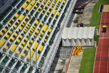 Kırmızı pistli yeşil futbol stadyumunda ön sıra sarı koltuk.