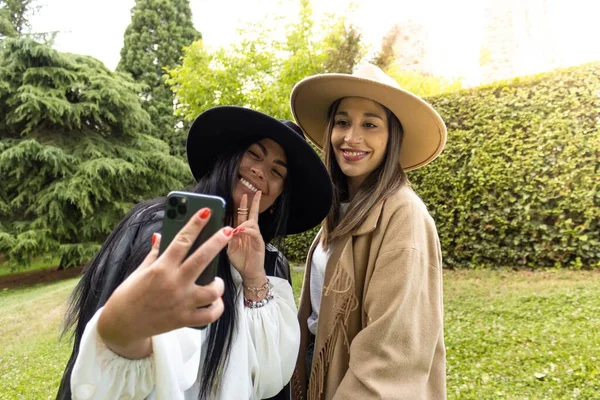 Portret Dwóch Uśmiechniętych Dziewczyn Kapeluszach Robiących Selfie Razem Parku Świetle — Zdjęcie stockowe