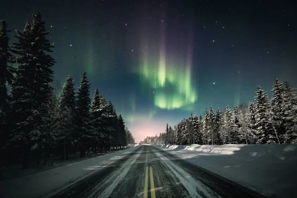 フィンランドのラップランドで雪に覆われたモミの森を通り過ぎる道路の上空の星空の中の極光 — ストック写真