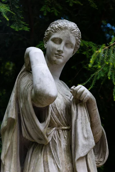 一个年轻女子的白色大理石雕像在绿树上垂直拍摄的照片 — 图库照片