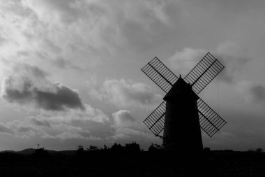 Kırsalda bulunan bir yel değirmeninin gri tonlu silueti.