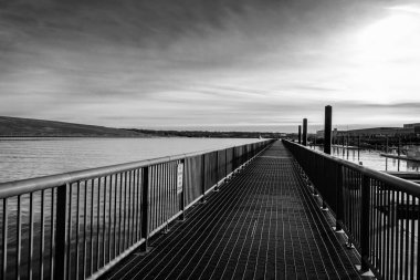 Kasvetli bir günde bulutlu bir gökyüzünün altında bir göl boyunca uzanan bir köprünün gri pulu.