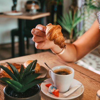 Bir kadın elinin kruvasanı bir fincan duble espresso üzerinde tutuşu.