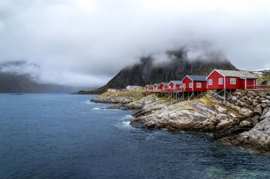 Norveç 'teki Lofoten takımadalarının manzarası. Gün ışığında önlerinde kırmızı kulübeler var.