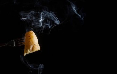 Çatalla kaplanmış, siyah arka planda dumanı olan tatlı bir patates