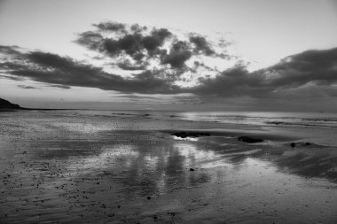 Bulutlu gökyüzünün durgun su yüzeyine yansıyan gri tonlu görüntüsü