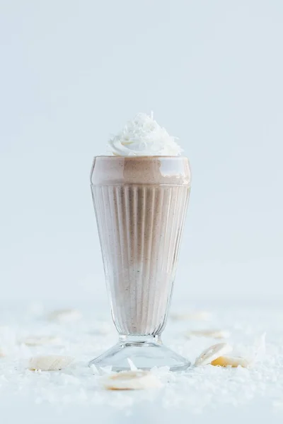 一杯巧克力奶昔与椰子片放在白桌上的垂直镜头 — 图库照片