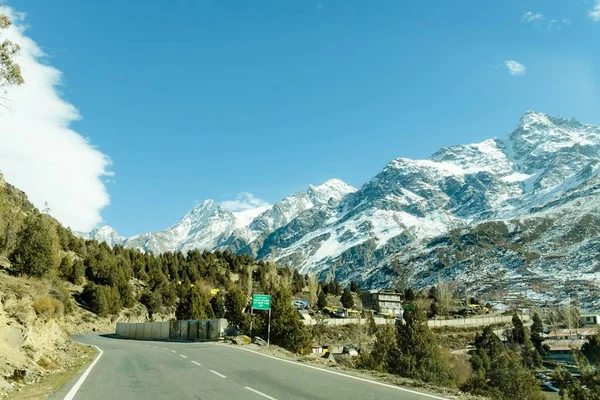 从沥青路面在山上覆盖着雪和路边 背景为蓝色的天空和云树景区冬季视图 — 图库照片