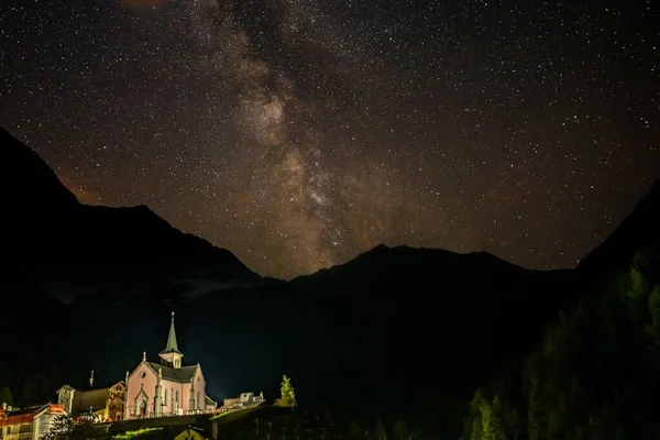 A beautiful view of the Trient Eglise Rose church in the Swiss Alps at night with a sky full of stars