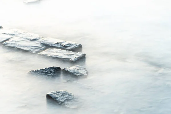 stock image A high angle of steam and snow covering the coastal stones on a cold winter day