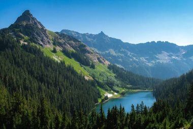 Su ve sık ağaçlarla çevrili dağ manzarası.