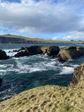 Bulutlu bir gökyüzünün altında kaya oluşumları olan bir deniz manzarasının dikey çekimi.