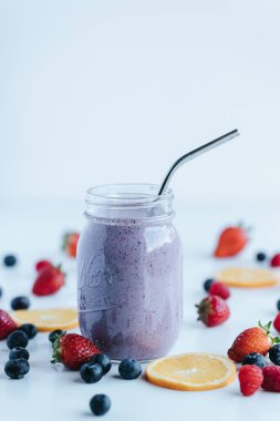 Beyaz arka planda meyvelerle çevrili bir bardak meyveli milkshake 'in dikey yakın çekimi.