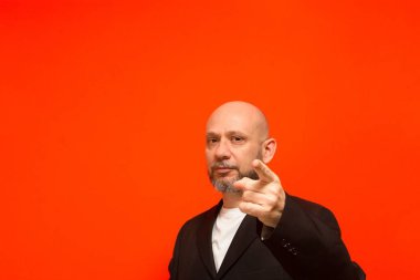 İş adamı, kel ve sakallı, zeki, kamerayı işaret ediyor. Turuncu arka planda izole edilmiş.