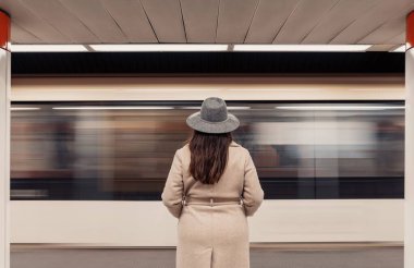 Hareket halindeki trenin önündeki metro peronunda duran kadının arka görüntüsü..