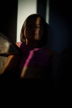 Perdelerin arkasından bakan beyaz bir kızın dikey görüntüsü.