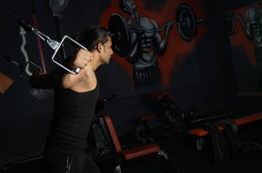 Güney Asyalı bir adam spor salonunda biceps yapıyor.