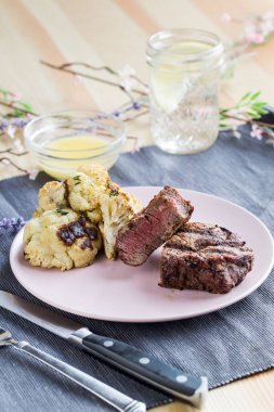 Biftek, beyaz bir tabakta, soslu ve mavi kumaşlı bir bardak suyla dikey bir çekim.