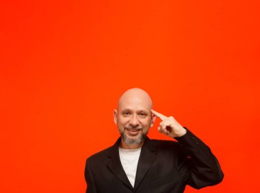 Siyah ceketli, zeki ve düşünceli bir iş adamı. Turuncu arka planda izole edilmiş.