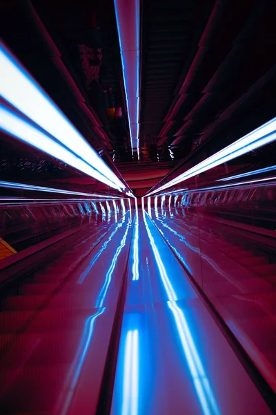 A vertical shot of light streaks formed by under-railing lighting on an escalator