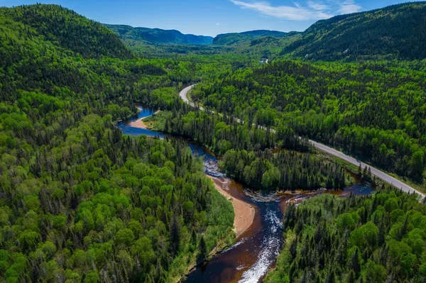 カナダのケベック州の曇り空の下 山を背景に木々と緑の間の狭い川と道路 — ストック写真