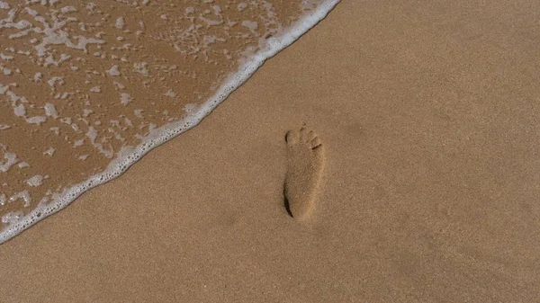 波が飛び散る砂のビーチの砂の上の足跡 — ストック写真
