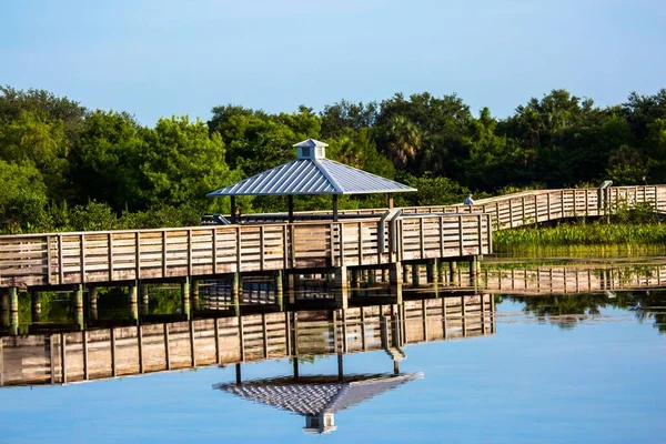 stock image A gazebo and boardwalk over a lake with reflections in the water