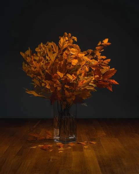 透明なガラスの花瓶の中に置かれたオレンジの葉の垂直ショット — ストック写真