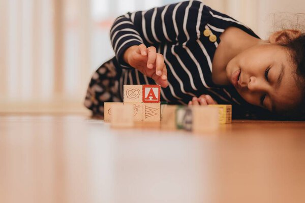 A preschool girl, lying on the hardwood floor at home, playing with wooden letter blocks, the concept of early education